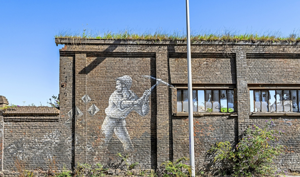 Wandgemälde eines Bergarbeiters mit Spitzhacke: Graffito an der Backsteinwand einer verlassenen Industrieanlage.
