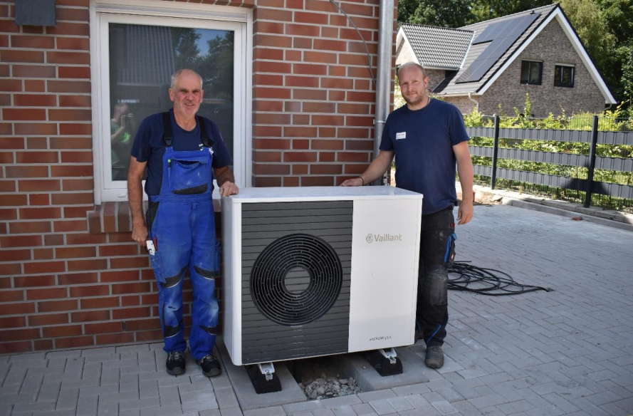 Ralf Wippig (1.) und Thorsten Wilken mit der frisch installierten Außeneinheit einer Wärmepumpe auf einer Baustelle in Schortens. BILD: Frank Brüling