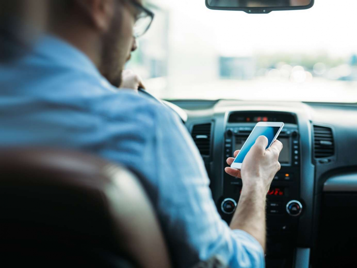 Mal eben schnell während der Fahrt auf das Handy schauen – weit verbreitet in Deutschland. Aber ist das wirklich zulässig? BILD: ERGO Group/Canva