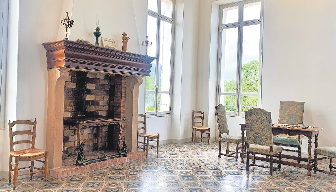 HÖLZERNE STILMÖBEL UND BODENKACHELN IM PROVENZALISCHEN STIL SCHMÜCKEN DIESEN LICHT DURCHFLUTETEN EHEMALIGEN WOHNRAUM MIT SEINEM KAMIN.
