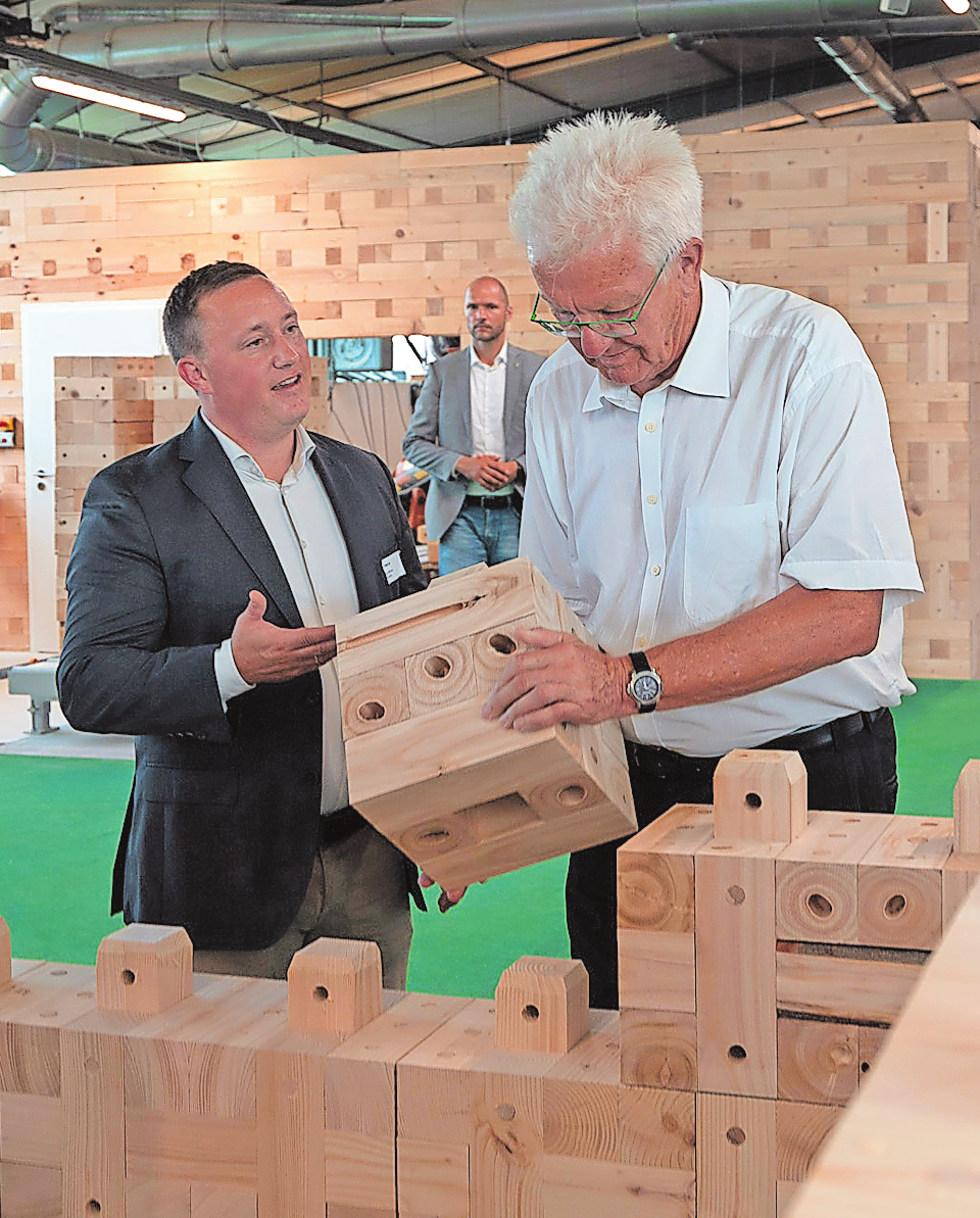DER BADEN-WÜRTTEMBERGISCHE MINISTERPRÄSIDENT WINFRIED KRETSCHMANN VERSUCHT SICH ALS „HOLZ-MAURER“, UND FIRMEN-VORSTAND MAX WÖRNER ASSISTIERT. FOTO: TRIQBRIQ