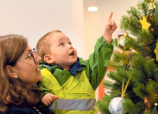 Der kleine Levi ist eines der Krippenkinder aus der Inklusiven Krippe Kleine Raupe. Hier schmücken er und Erzieherin Jessica Kasper den Weihnachtsbaum in der UR Bank Wittorf.
