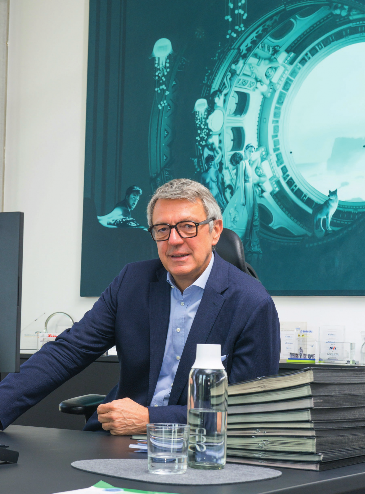 Arndt Geiwitz vor einem akkuraten Aktenstapel, eine großformatige Arbeit von Kristian Evju im Hintergrund. Foto: Marc Hörger