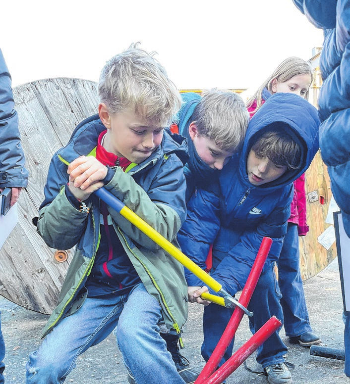 Drei Schüler beim Versuch, ein Kabelstück mit einer speziellen Zange abzuschneiden.