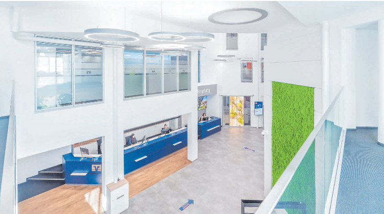 Ein Blick von oben auf die neue Kundenhalle, die in weiß gehalten ist, aber mit der blauen Servicetheke und den grünen Mooswänden Farbakzente setzt.