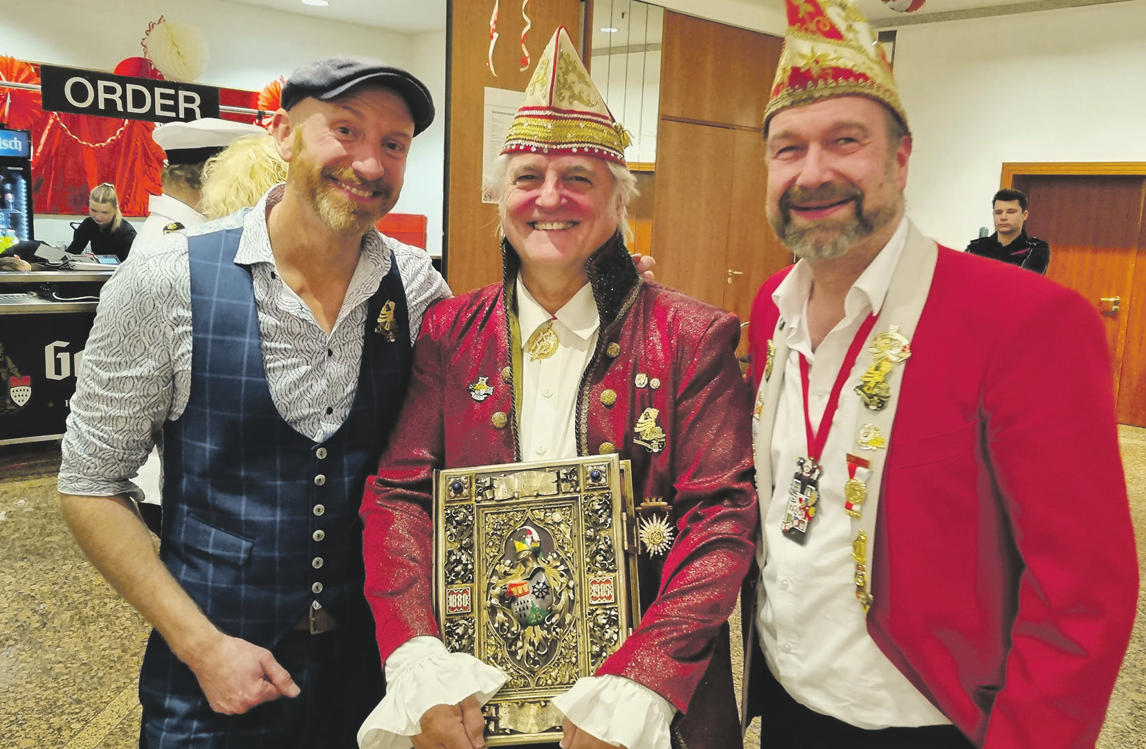 Der Archivar der Kölner Narren-Zunft, Helmut Trum (M.), mit dem Goldenen Buch der Gesellschaft sowie den Rednern Martin Schopps (I.) und Sitzungspräsident Volker Weininger Bild: KNZ