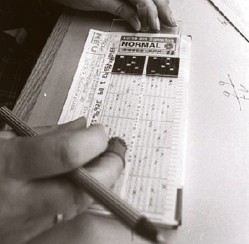 Handwerkszeug der Lotto-Auswertung in den frühen Jahren: Auswertungsschablonen (hinten) und gummierte Noppenfingerhüte, die beim Blättern halfen. Fehlerhafte Spielscheine, zum Beispiel mit sieben Kreuzen, konnte die Auswertungsmaschine nicht lesen und mussten deshalb manuell bearbeitet werden.