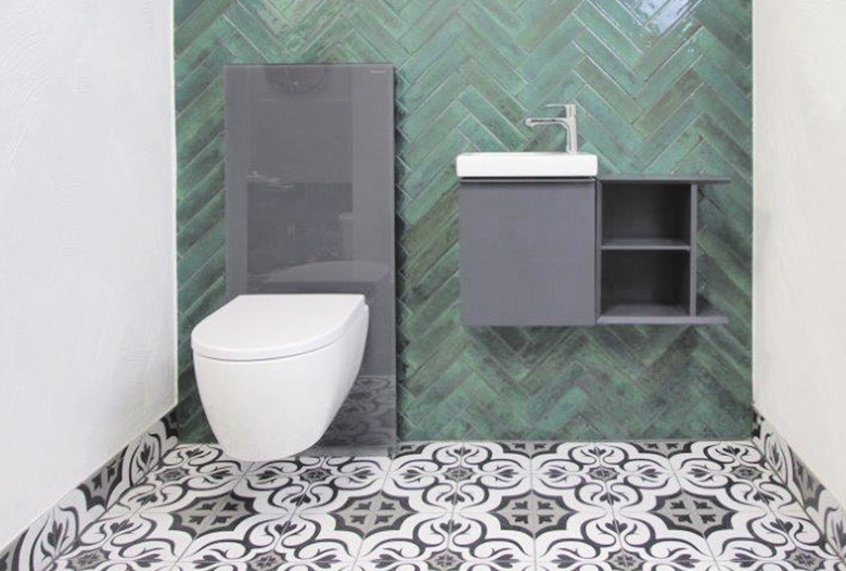 Stilvolles Gäste-WC mit grün glasierter Fliesenwand und gemustertem Boden.
