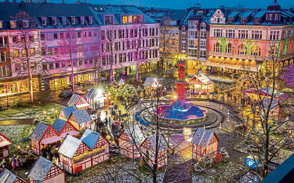 Der Görresplatz zeigt sich aus der Vogelperspektive als kleines weihnachtliches Dorf mit beleuchteten Hütten, farbig inszenierten Fassaden und dem Brunnen im Mittelpunkt. Foto: Koblenz-Touristik GmbH Henry Tornow