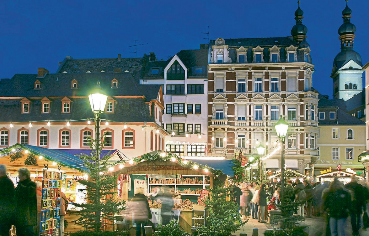 Der Münzplatz präsentiert sich mit dicht gereihten Ständen und kunstvollen Holzarbeiten, eingerahmt von historischen Häuserzeilen und warmem Lichterglanz. Foto: Koblenz-Touristik GmbH / gauls DIE FOTOGRAFEN