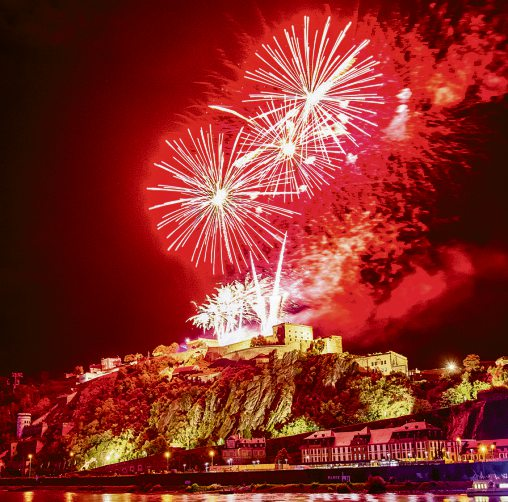 Leuchtende Feuerwerksbilder über der Festung Ehrenbreitstein spiegeln sich im Rhein und tauchen das Ufer in kräftiges Rot. Foto: Koblenz-Touristik/Johannes Bruchhof