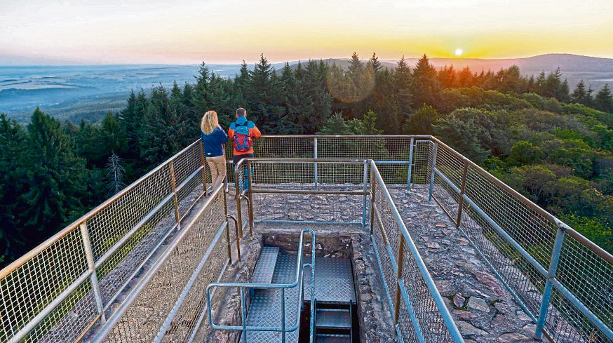 Von der Burgruine Koppenstein aus genießen Wanderer bei Sonnenuntergang einen weiten Rundumblick über die Hunsrück-Hochebene.