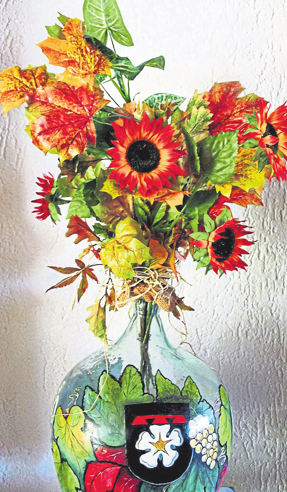 Herbstlicher Schmuck mit Ortsbezug: Das Layer Wappen ziert den Glasballon, der als Vase für den farbenfrohen Strauß dient.