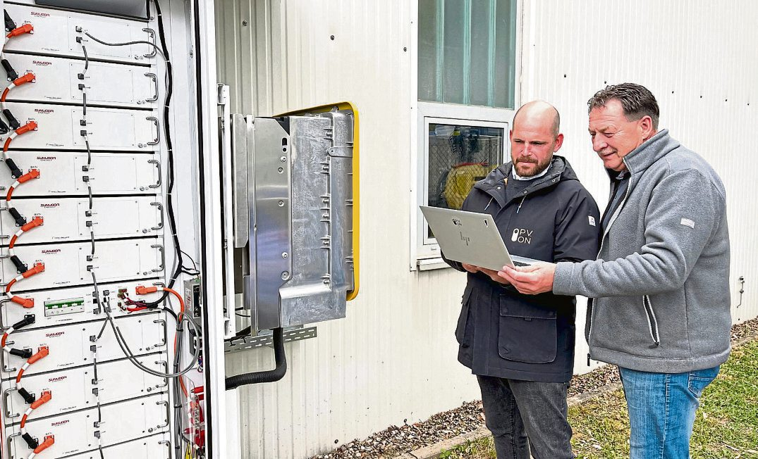 Tim Schossig, Geschäftsführer von PV.ON, und Stefan Ermel, Abteilungsleiter Facility Management der Kreuznacher Stadtwerke, am neuen Batteriespeicher. Die Anlage speichert bis zu 120 Kilowattstunden Strom aus der Photovoltaikanlage des Logistikzentrums und macht ihn zeitversetzt nutzbar. Dadurch stieg der Eigenverbrauchsanteil des erzeugten Solarstroms von 67 auf 94 Prozent. Foto: Lea Agsten