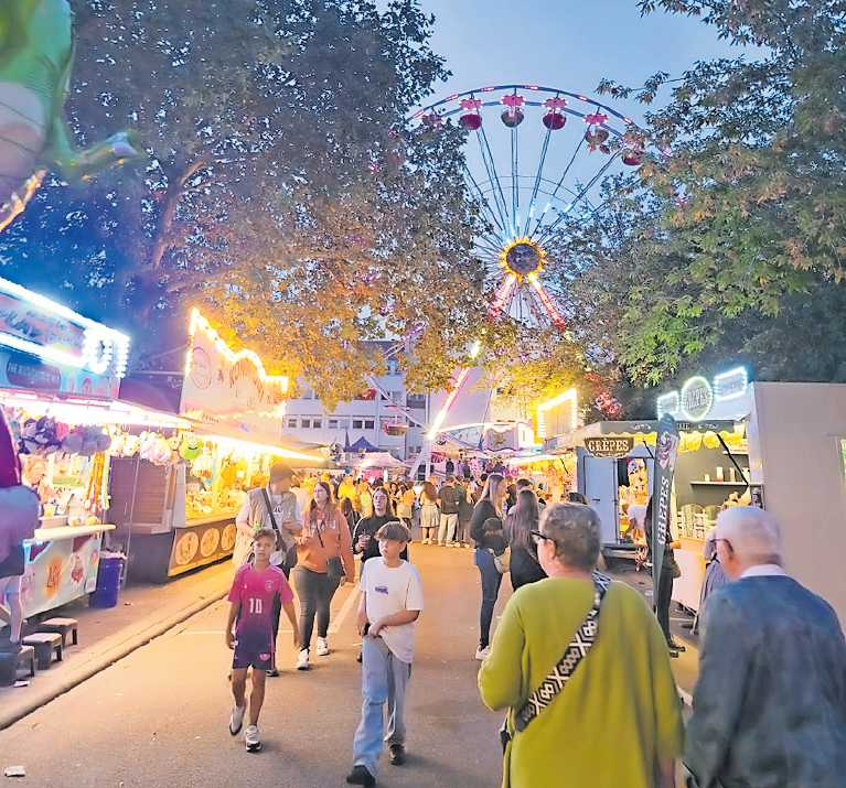 Festplatz mit Fahrgeschäften, dahinter das Riesenrad